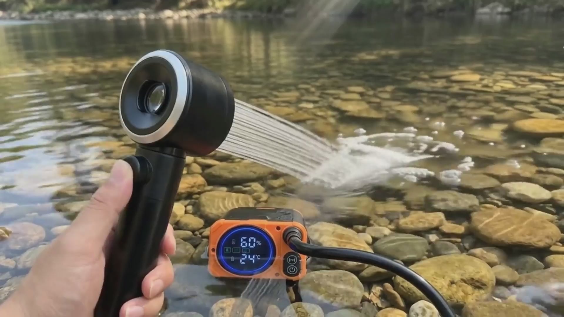 Terra Rinse Pro portable camping shower pump submerged in a crystal-clear outdoor river stream, demonstrating a powerful tactical water spray over smooth river stones.
